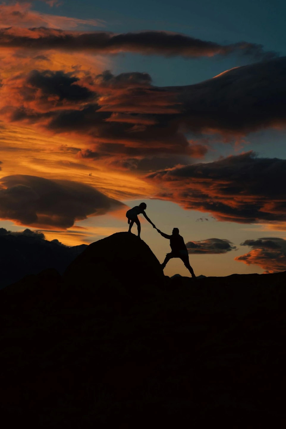 one person grabbing another person's hand, helping them up a hill
